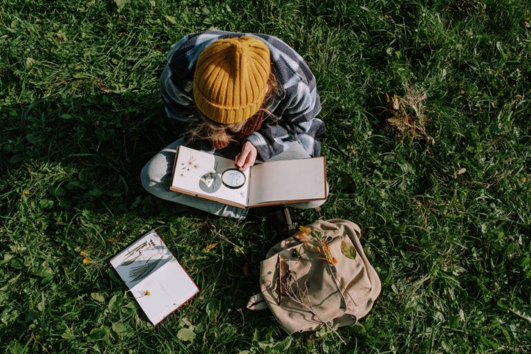 A person explores flora outdoors using a magnifying glass, surrounded by nature and greenery.